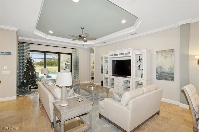 living room with a raised ceiling, ceiling fan, and ornamental molding