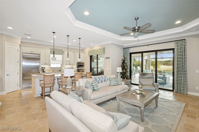 living room featuring a raised ceiling, ceiling fan, and ornamental molding