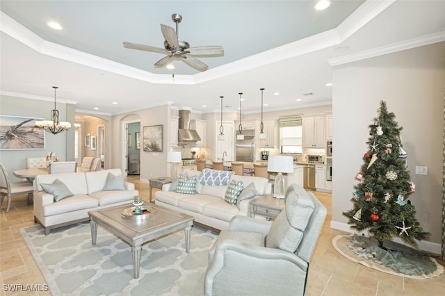 living room with a raised ceiling, ceiling fan with notable chandelier, and ornamental molding