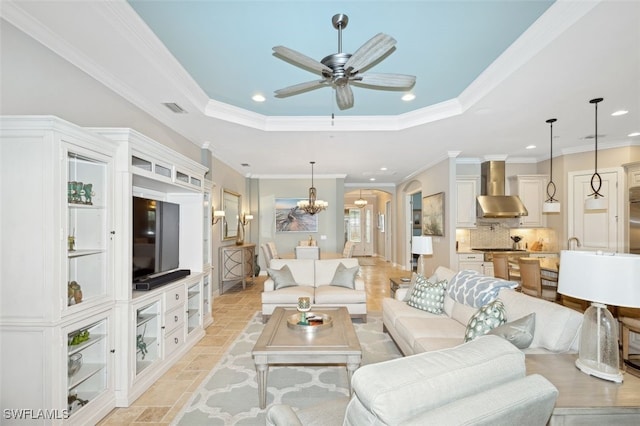 living room with ceiling fan with notable chandelier, a raised ceiling, and ornamental molding