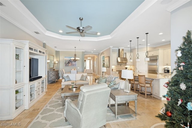 living room with ceiling fan with notable chandelier, a raised ceiling, and ornamental molding