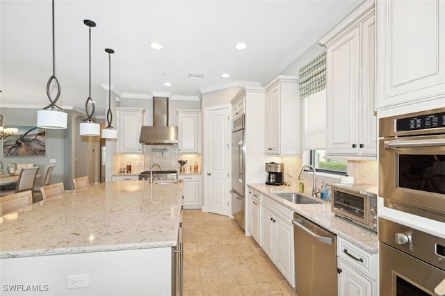 kitchen featuring wall chimney exhaust hood, white cabinetry, sink, and decorative light fixtures