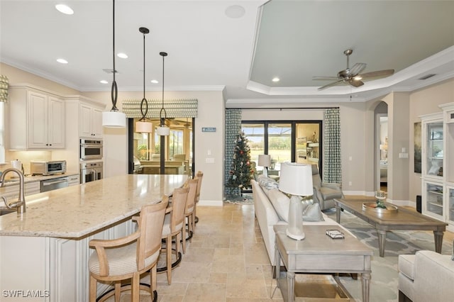 kitchen with appliances with stainless steel finishes, light stone counters, a raised ceiling, ceiling fan, and decorative light fixtures