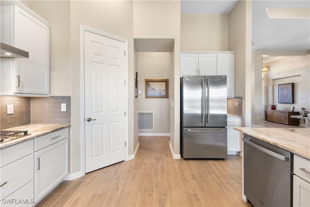 kitchen with white cabinets, light stone counters, stainless steel appliances, and light hardwood / wood-style flooring