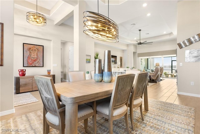 dining space featuring ceiling fan with notable chandelier, light wood-type flooring, a towering ceiling, and a tray ceiling