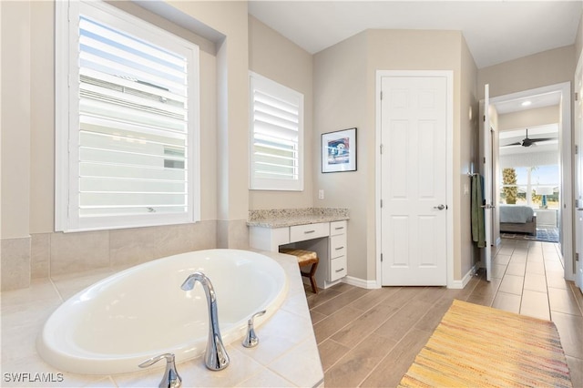 bathroom featuring hardwood / wood-style floors, a relaxing tiled tub, ceiling fan, and vanity