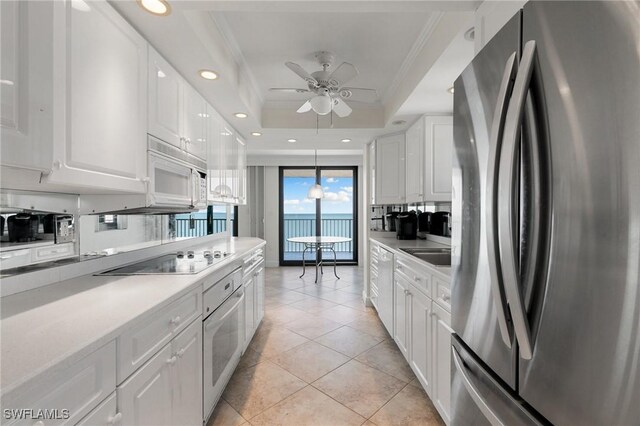 kitchen with white appliances, a tray ceiling, ceiling fan, light tile patterned floors, and white cabinets