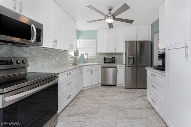 kitchen with light stone countertops, tasteful backsplash, stainless steel appliances, sink, and white cabinets