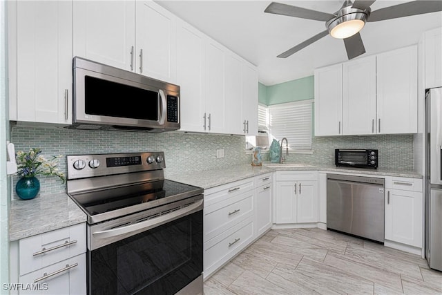 kitchen with tasteful backsplash, light stone counters, stainless steel appliances, sink, and white cabinets