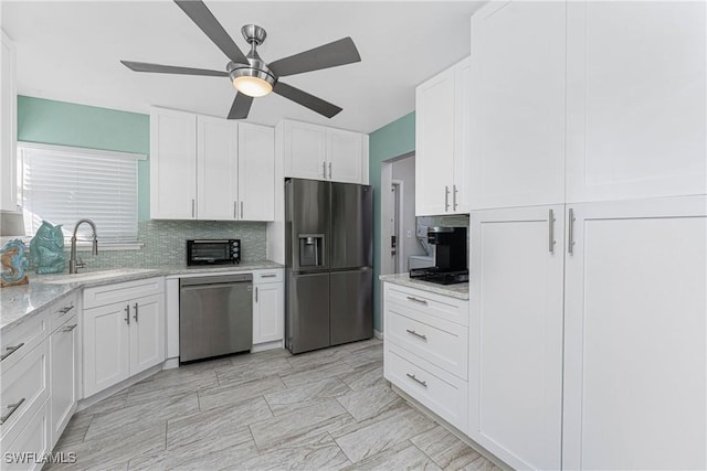 kitchen featuring backsplash, white cabinets, sink, appliances with stainless steel finishes, and light stone counters