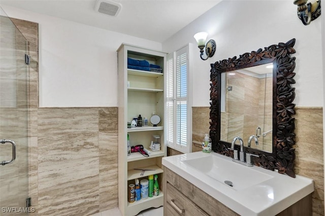 bathroom with vanity, a shower with door, and tile walls