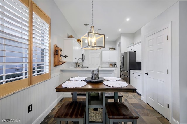 dining area with recessed lighting, stone finish flooring, wainscoting, and an inviting chandelier