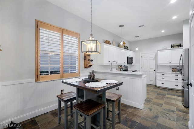 kitchen with a peninsula, stone finish floor, wainscoting, and stainless steel appliances