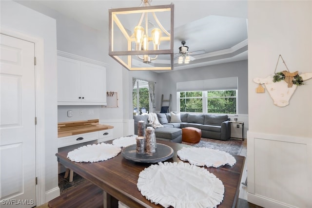 dining area featuring a wainscoted wall, an inviting chandelier, dark wood-style flooring, and a raised ceiling