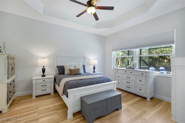 bedroom featuring a raised ceiling, multiple windows, light wood-style floors, and baseboards