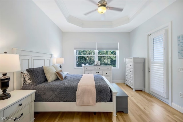 bedroom featuring light wood finished floors, baseboards, a tray ceiling, and ornamental molding