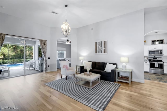 living room with ceiling fan, a towering ceiling, and light hardwood / wood-style flooring