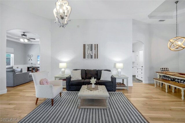 living room featuring a raised ceiling, ceiling fan with notable chandelier, and light hardwood / wood-style flooring