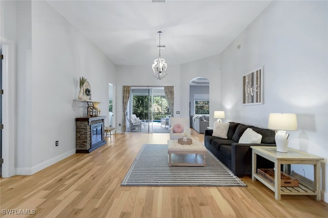 living room with a towering ceiling, arched walkways, light wood finished floors, baseboards, and a chandelier