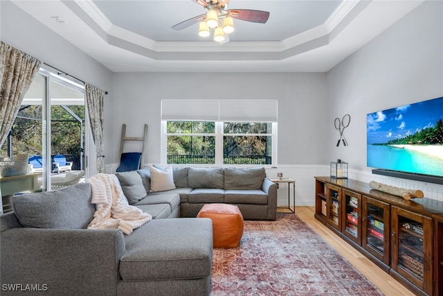 living room featuring light wood-type flooring, a wealth of natural light, a raised ceiling, and crown molding