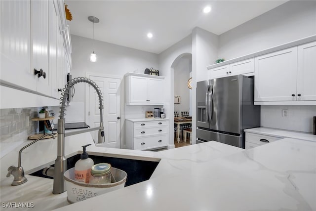 kitchen featuring white cabinetry, stainless steel fridge, backsplash, and light stone countertops