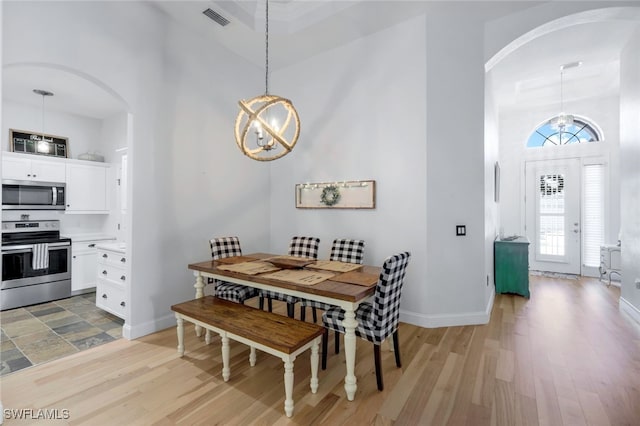 dining room with light wood-style flooring, a notable chandelier, visible vents, and arched walkways