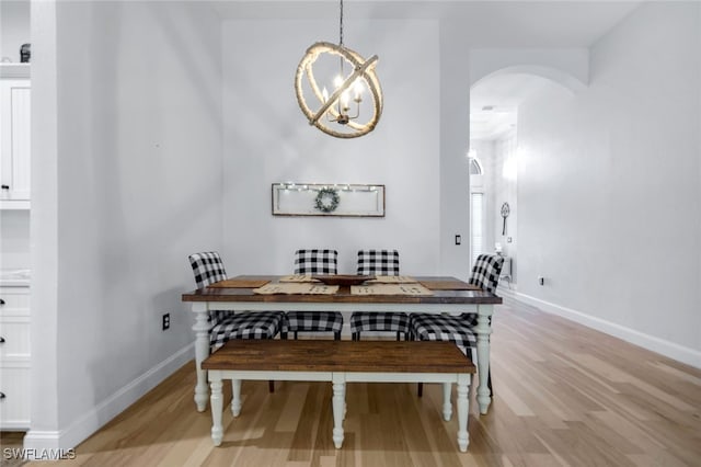 dining area featuring arched walkways, a chandelier, light wood finished floors, and baseboards