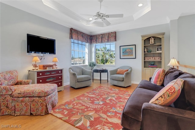 living room featuring light hardwood / wood-style flooring, a raised ceiling, ceiling fan, and ornamental molding