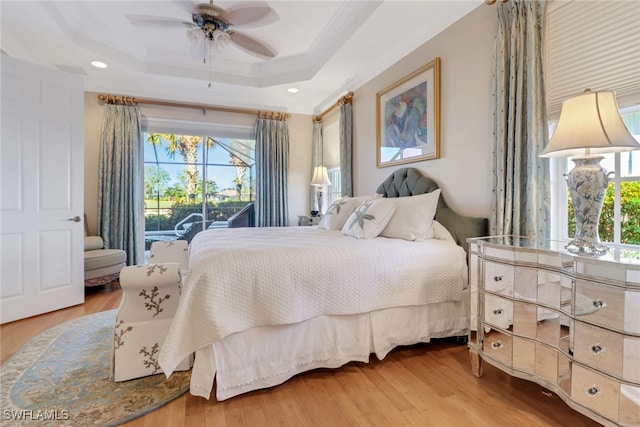 bedroom featuring hardwood / wood-style floors, ceiling fan, a tray ceiling, and multiple windows