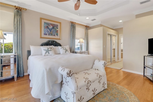 bedroom with a raised ceiling, ceiling fan, ornamental molding, and light wood-type flooring