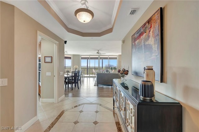 hallway featuring a tray ceiling, light tile patterned flooring, and ornamental molding