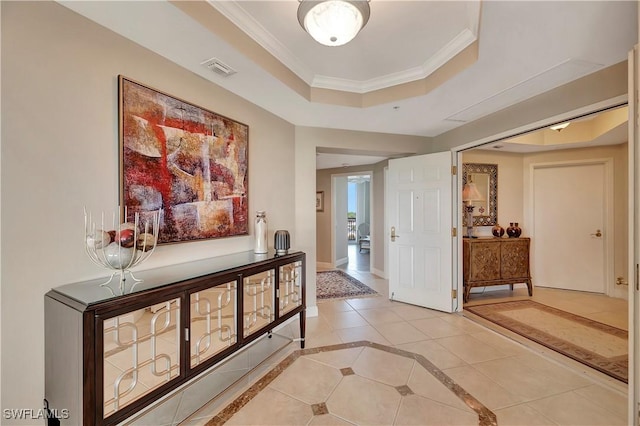 corridor featuring ornamental molding, light tile patterned floors, and a tray ceiling