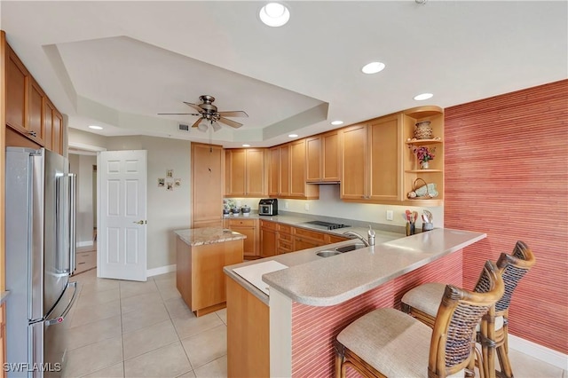 kitchen featuring ceiling fan, a kitchen breakfast bar, cooktop, kitchen peninsula, and stainless steel fridge