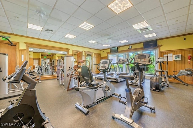 gym featuring ornamental molding, a drop ceiling, and wooden walls