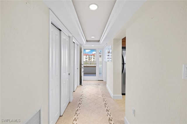 hallway with light tile patterned flooring and a tray ceiling