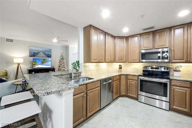 kitchen with ceiling fan, sink, kitchen peninsula, decorative backsplash, and appliances with stainless steel finishes