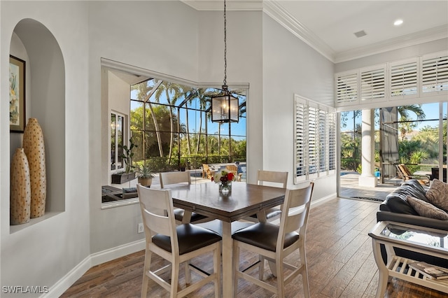 dining area with a towering ceiling, ornamental molding, a notable chandelier, and hardwood / wood-style flooring