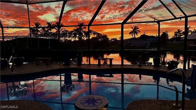 pool at dusk with glass enclosure, a patio area, and a water view