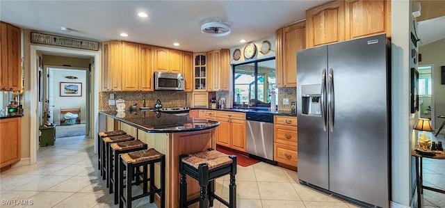 kitchen with appliances with stainless steel finishes, a breakfast bar, glass insert cabinets, and light tile patterned floors