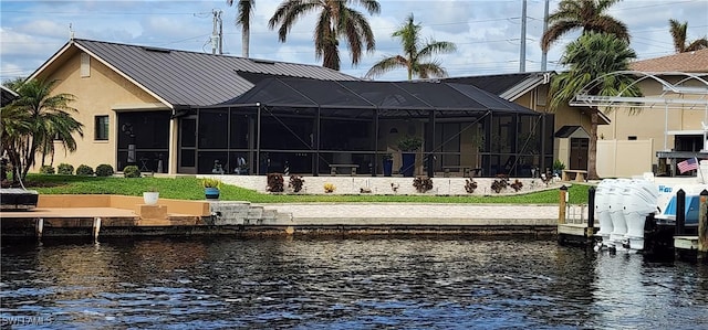 back of property featuring stucco siding, metal roof, glass enclosure, and a water view