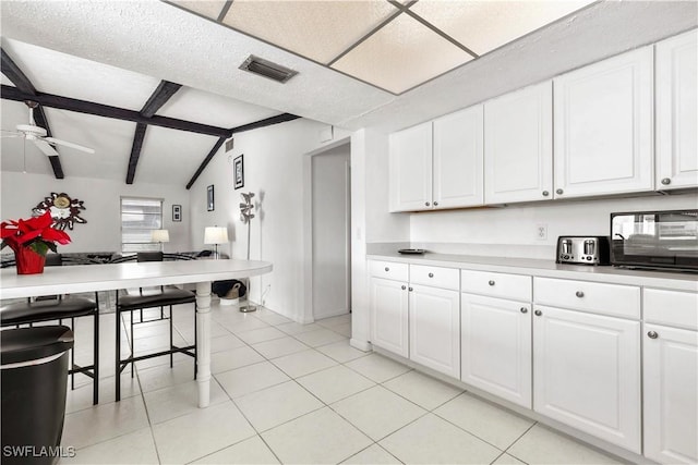 kitchen featuring white cabinetry, vaulted ceiling with beams, light tile patterned floors, and ceiling fan