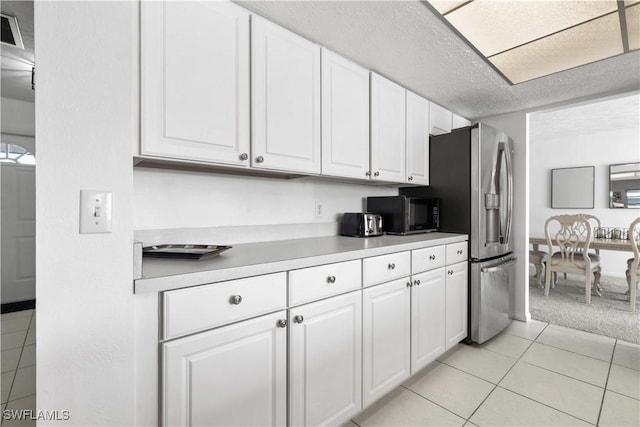 kitchen with light tile patterned floors, stainless steel fridge, and white cabinets