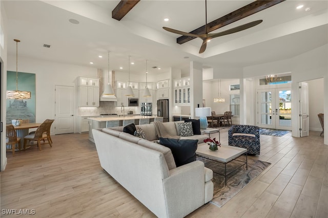 living room with beam ceiling, light wood-type flooring, and french doors