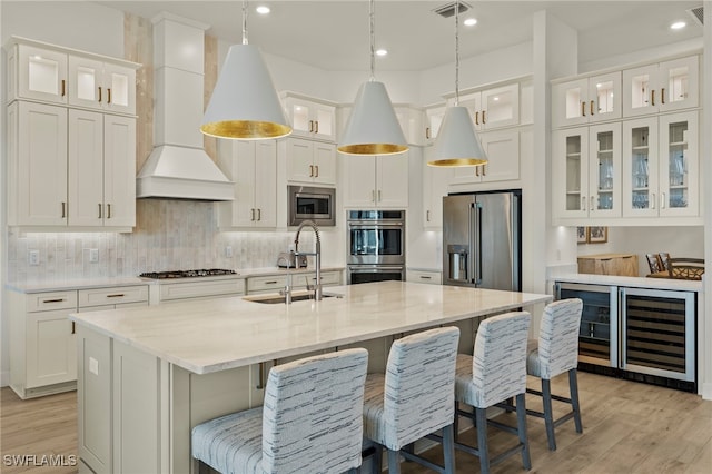 kitchen featuring white cabinetry, a center island with sink, custom exhaust hood, and appliances with stainless steel finishes