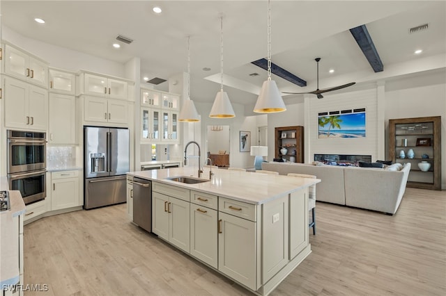 kitchen featuring sink, stainless steel appliances, light stone counters, light hardwood / wood-style flooring, and a center island with sink