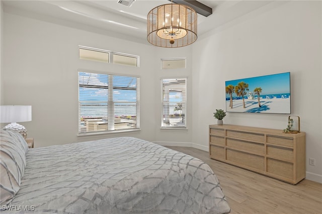 bedroom with beam ceiling, a high ceiling, and light wood-type flooring