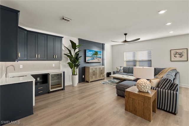 living room with ceiling fan, sink, wine cooler, and light hardwood / wood-style flooring