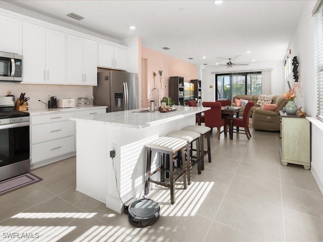 kitchen with a center island with sink, ceiling fan, white cabinetry, and stainless steel appliances