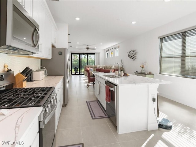 kitchen with stainless steel appliances, a kitchen island with sink, ceiling fan, sink, and white cabinets