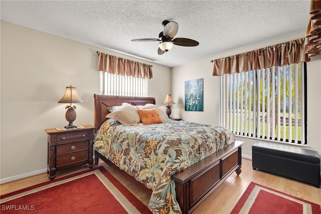 bedroom with ceiling fan, wood-type flooring, a textured ceiling, and multiple windows